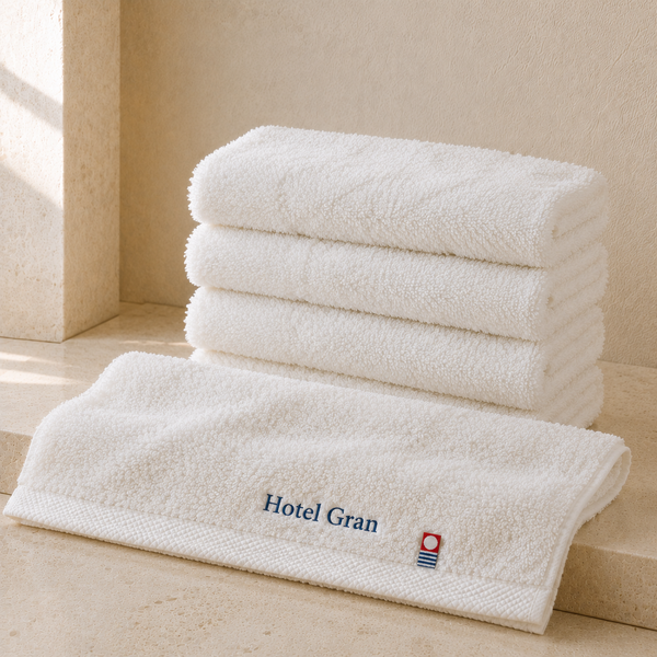 重ねた白い今治フェイスタオルと、紺色の糸で「Hotel Gran」と刺繍され今治タオルのマークが付いた1枚